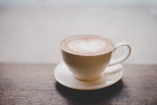 Vintage latte art coffee with heart shape on wooden table.