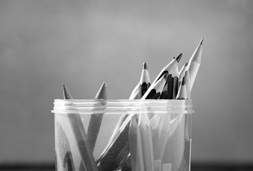 Close up of Colored pencils are in a plastic round box placed on a wooden table by the window. Black and white style tone.