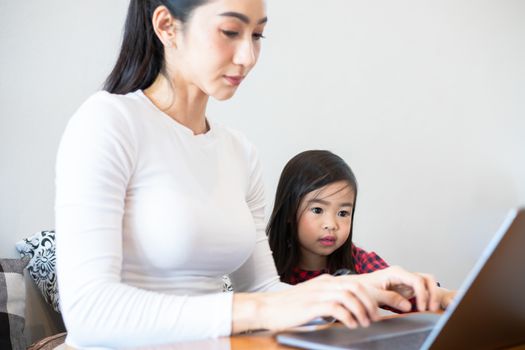 Asian mothers are teaching their daughters to read a book and use notebooks and technology for online learning during school holidays at home. Educational concepts and activities of the family
