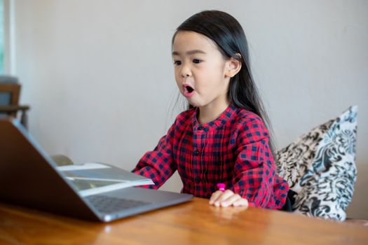 Asian girl or daughters use notebooks and technology for online learning during school holidays and watching cartoons at home. Educational concepts and activities of the family