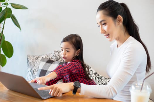 Asian mothers are teaching their daughters to read a book and use notebooks and technology for online learning during school holidays at home. Educational concepts and activities of the family