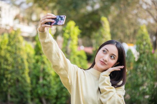 Cute Asian women are using their phones to take selfies and smile happy in the garden at home.