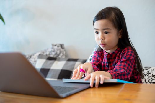 Asian girl or daughters use notebooks and technology for online learning during school holidays and watching cartoons at home. Educational concepts and activities of the family