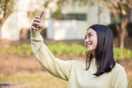 Cute Asian women are using their phones to take selfies and smile happy in the garden at home.
