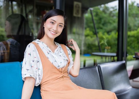 Cute Asian woman sits on the sofa or chair and looks at the camera and smiles happy in portraits at home during relax time.