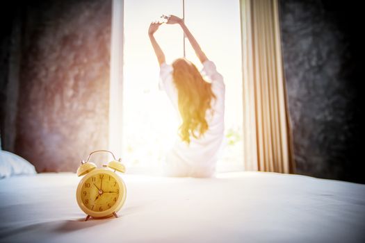 alarm clock having a good day of Asian woman waking up in her bed fully rested and open the curtains in the morning to get fresh air at home