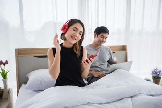 The couple put on their headphones and listened to music on their mobile phones on the couch and they were dancing happy in the house for social distance and self responsibility concept