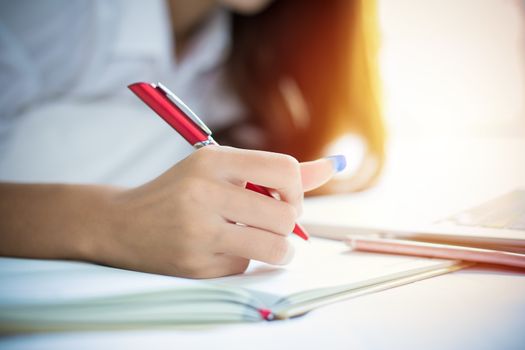 Asian woman is using a pen to write notes in her notebook and she uses a notebook to work on her bed at home.
