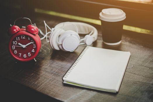 Paper cup of coffee,notebook and Red alarm clock with headphone on the wood table, Relaxing time. Lifestyle concept. 