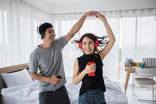 The couple put on their headphones and listened to music on their mobile phones on the couch and they were dancing happy in the house for social distance and self responsibility concept