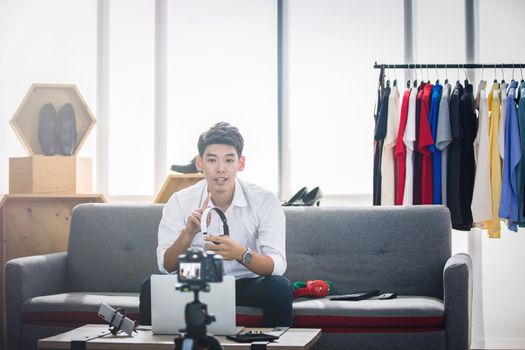 Asian man blogger broadcasting a video for selling product online such as Hats, shoes, headphones, clothing, safety headers.Shopping online concept  at home