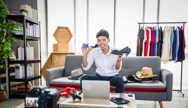 Asian man blogger broadcasting a video for selling product online such as Hats, shoes, headphones, clothing, safety headers.Shopping online concept  at home