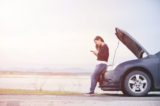 Asian woman is using a telephone to call the car mechanic. For fixing damaged cars on the road