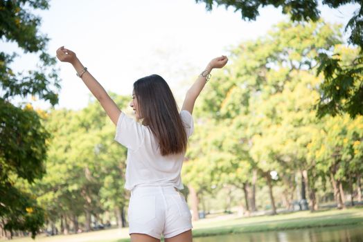 Portrait of teenage girl raising arms and laughing in the park.