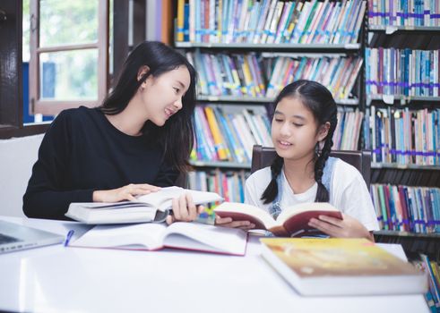Two Asian girl students reading books and using notebook in the library.