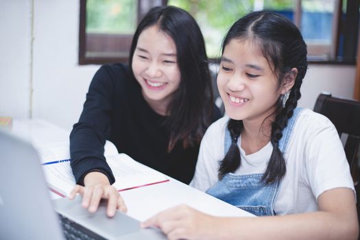 Two Asian girl students reading books and using notebook in the library.