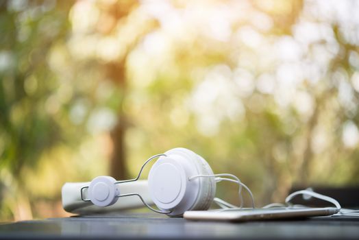 Mobile phone with headphone on wooden table with nature background - Vintage Filter.