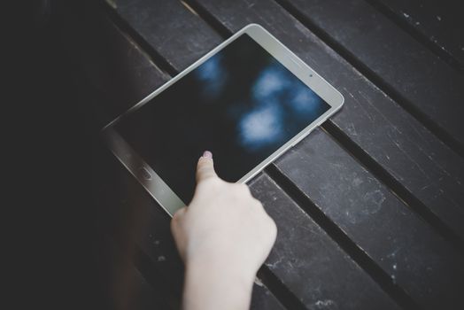 Close up of woman hands holding tablet computer on the wooden table with cup of coffee.