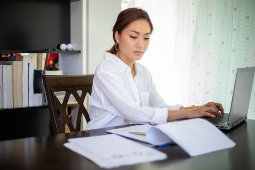 Beautiful Asian business women checking document and using notebook working from home for social distance and self responsibility concept