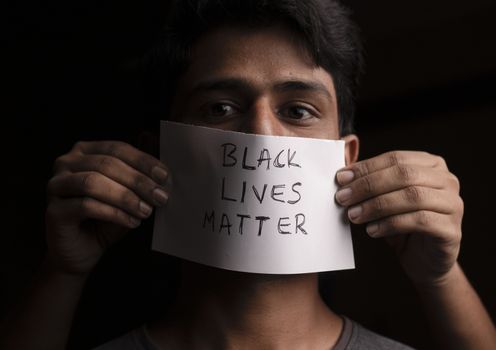 Young man's face covered with Black Lives Matter paper poster - concept of racial discrimination against black people