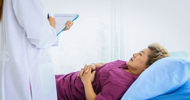 Doctor meeting and explaining medication to old woman patient lying in bed at Hospitals