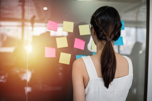 Asian business women smiling and Business people meeting at office and use post it notes to share idea. Brainstorming concept. Sticky note on glass wall.