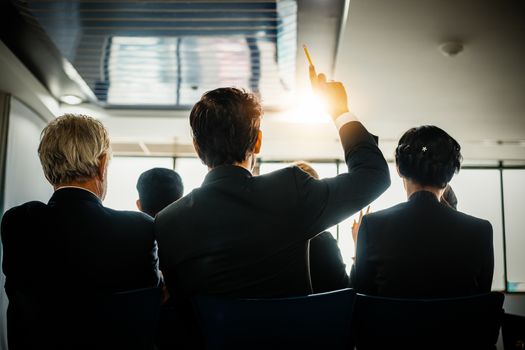 Business Audience raising hand up while businessman is speaking in training for Opinion with Meeting Leader in Conference Room