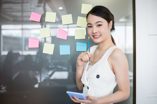 Asian business women smiling and Business people meeting at office and use post it notes to share idea. Brainstorming concept. Sticky note on glass wall.