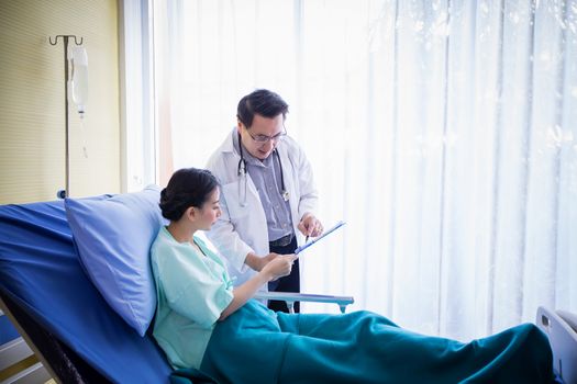 The doctors are asking and explaining about the illness to a female patient lying in bed at a hospital.