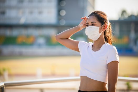 Asian Young fitness sport woman is resting tired and she wears a mask for protective Dust and pollution on city