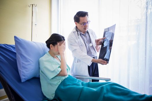 The doctor is explaining about the brain X-ray results to a female patient lying in bed at a hospital