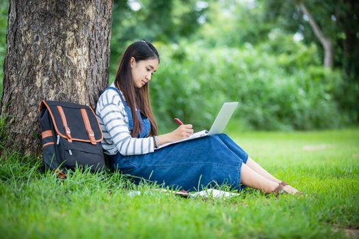 beautiful Asian girl student holding books and smiling at camera and learning and education concept  on park in summer for relax time