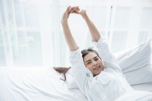 Asian woman Beautiful young smiling woman sitting and sleeping in white bed and stretching in the morning at bedroom after waking up in her bed fully rested