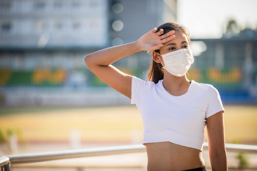 Asian Young fitness sport woman is resting tired and she wears a mask for protective Dust and pollution on city