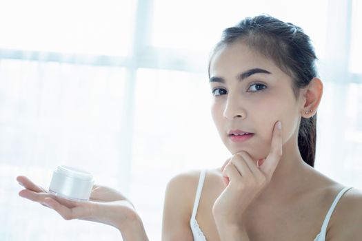 A beautiful woman asian using a skin care product, moisturizer or lotion taking care of her dry complexion. Moisturizing cream in female hands .