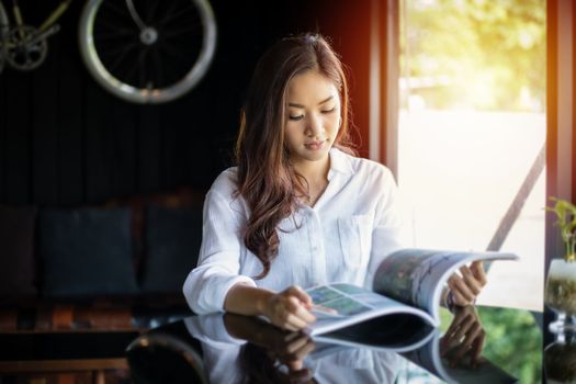 Asian women smiling and reading a book for relaxation at coffee shop