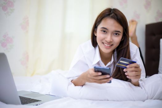 Asian women shopping online and paying with credit card on mobile phone. and Happy women at home surfing the net in bed