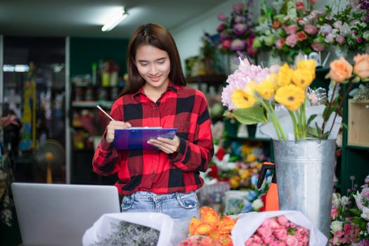 Asian Woman Florist Small Business Flower Shop Owner and She is using her telephone and laptop to take orders for her store.