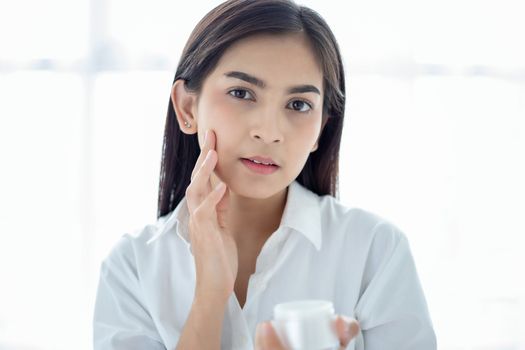 A beautiful woman asian using a skin care product, moisturizer or lotion taking care of her dry complexion. Moisturizing cream in female hands .