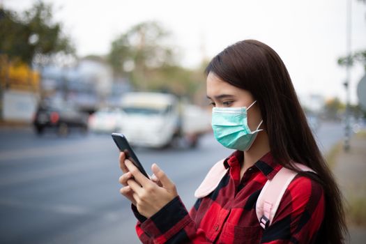 Asian Young woman using smart phone in the city wearing face mask because of air pollution, particulates and for protection flu virus, influenza, coronavirus
