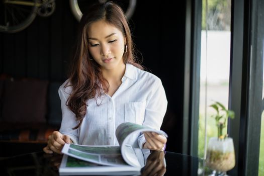 Asian women smiling and reading a book for relaxation at coffee shop