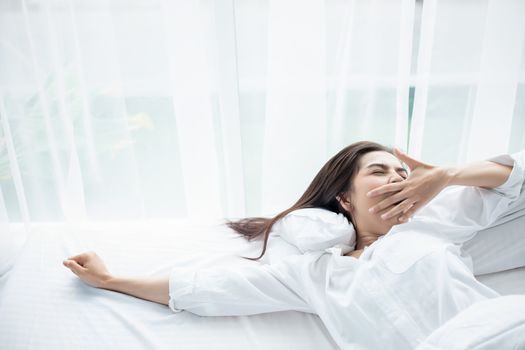 Asian woman Beautiful young smiling woman sitting and sleeping in white bed and stretching in the morning at bedroom after waking up in her bed fully rested