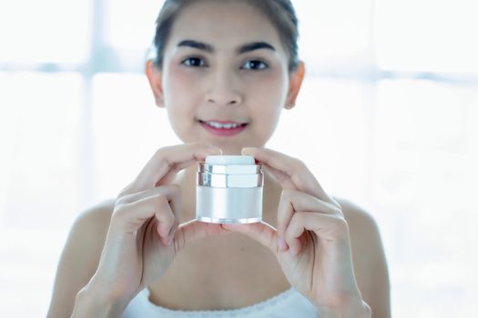 A beautiful woman asian using a skin care product, moisturizer or lotion taking care of her dry complexion. Moisturizing cream in female hands .