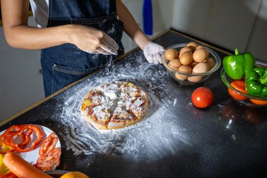 Asian women preparing a pizza, knead the dough and puts ingredients on kitchen table