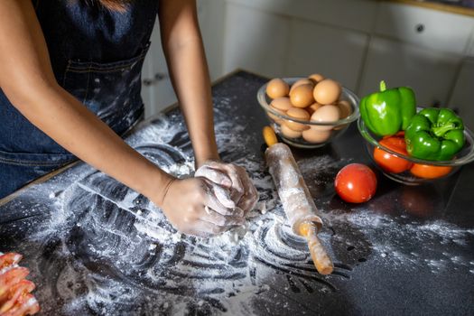 Asian women preparing a pizza, knead the dough and puts ingredients on kitchen table