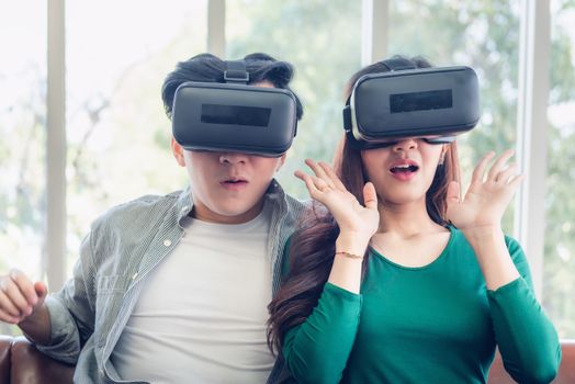 Young Couple Having Fun While Watching Video Via Virtual Reality Together. Couple Love Having Enjoyment With Electronic VR Goggles Gaming on Couch. Entertainment Innovation/Lifestyles Concept