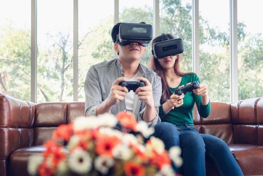 Young Couple Having Fun While Playing Virtual Reality Game Together in Their Home. Couple Love Having Enjoyment With Electronic VR Goggles Gaming on Couch. Entertainment Innovation/Lifestyles Concept