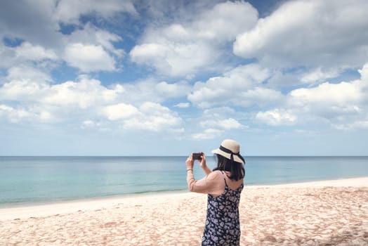 Portrait of Asian Woman is Using Mobile Phone for Capturing Natural Scenery at The Beach, Beautiful Woman is Having Fun and Enjoying With Her Phone in Summer Vacation on The Beach. Relaxing Lifestyles