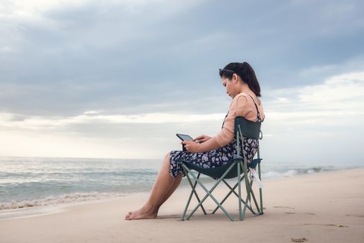 Freelancer Woman is Working on Tablet While Travel Vacation Trip at The Beach, Smart Woman is Using Tablet for Communication and Entertainment at Outdoor Sand Beach. Freelance and Relaxation Concept.