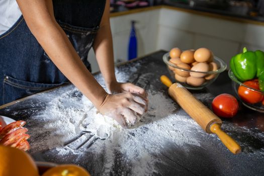 Asian women preparing a pizza, knead the dough and puts ingredients on kitchen table